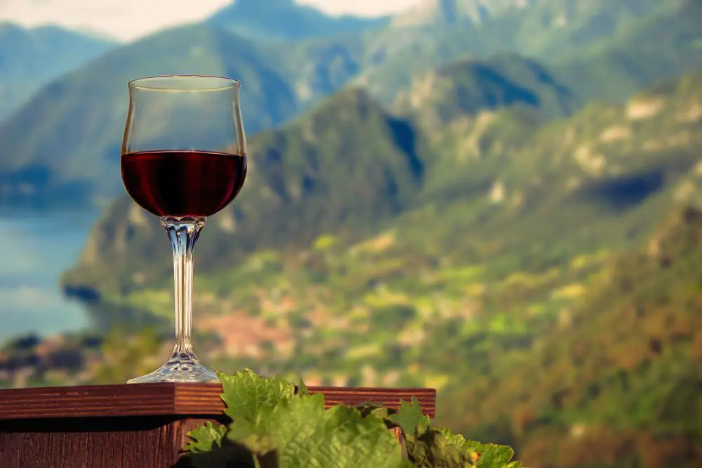 Close up of a glass of red wine infront of a view of Lake Garda and its mpuntains
