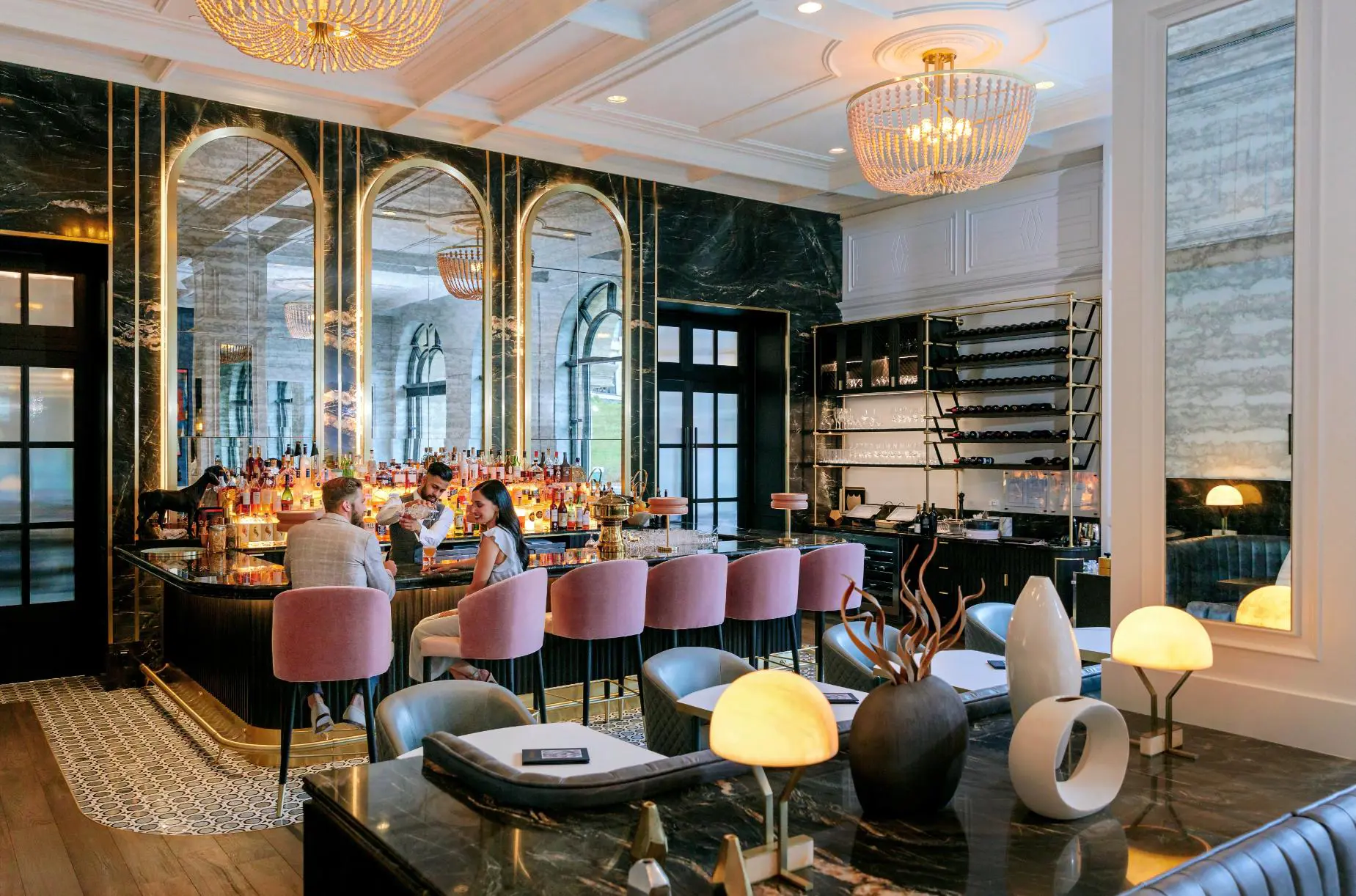Stylish hotel bar at Fairmont Chateau with pink velvet stools, guests enjoying drinks, and a luxurious ambience