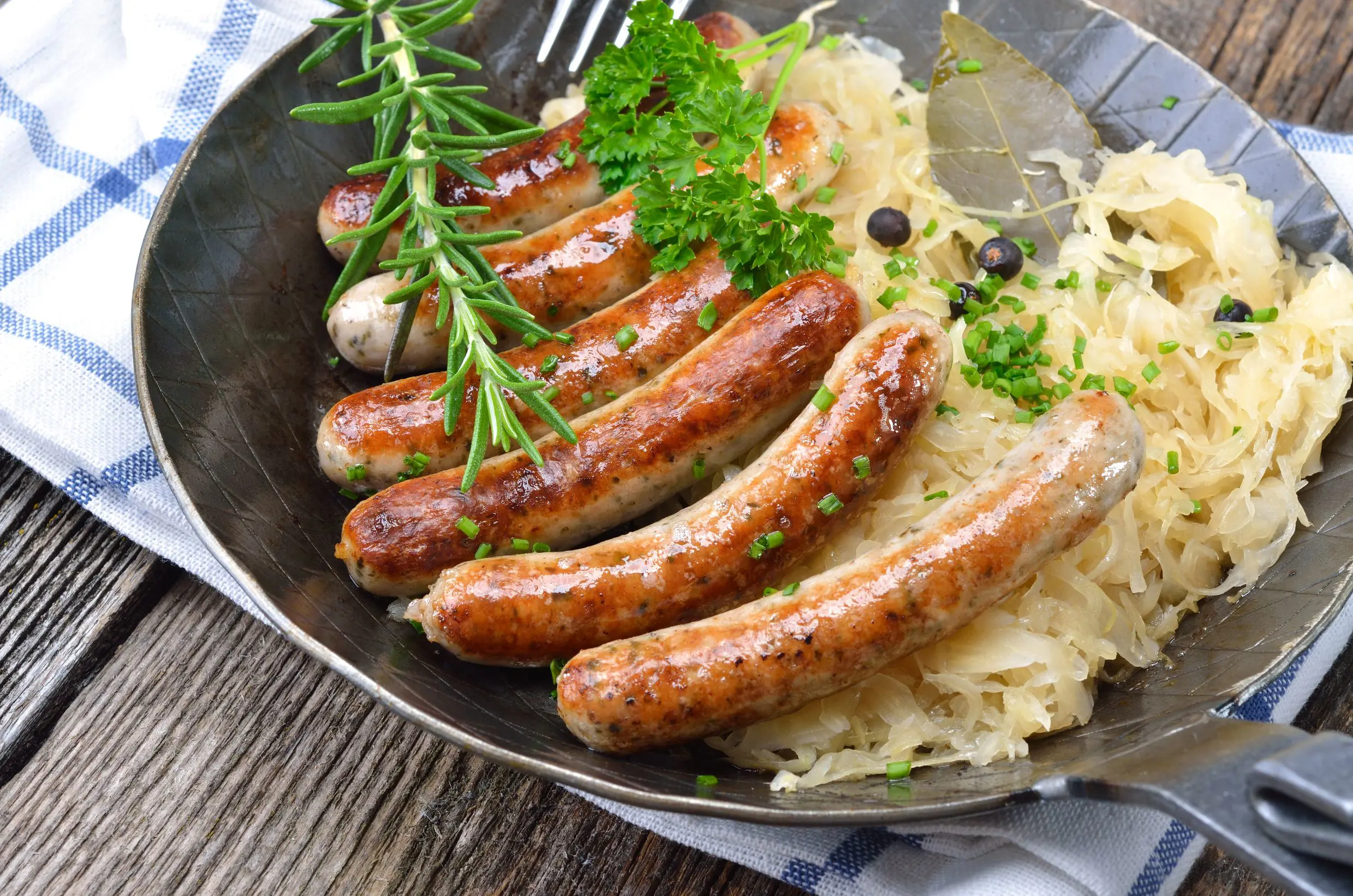 Plate of traditional German bratwurst and sauerkraut on a white and blue checkered cloth.