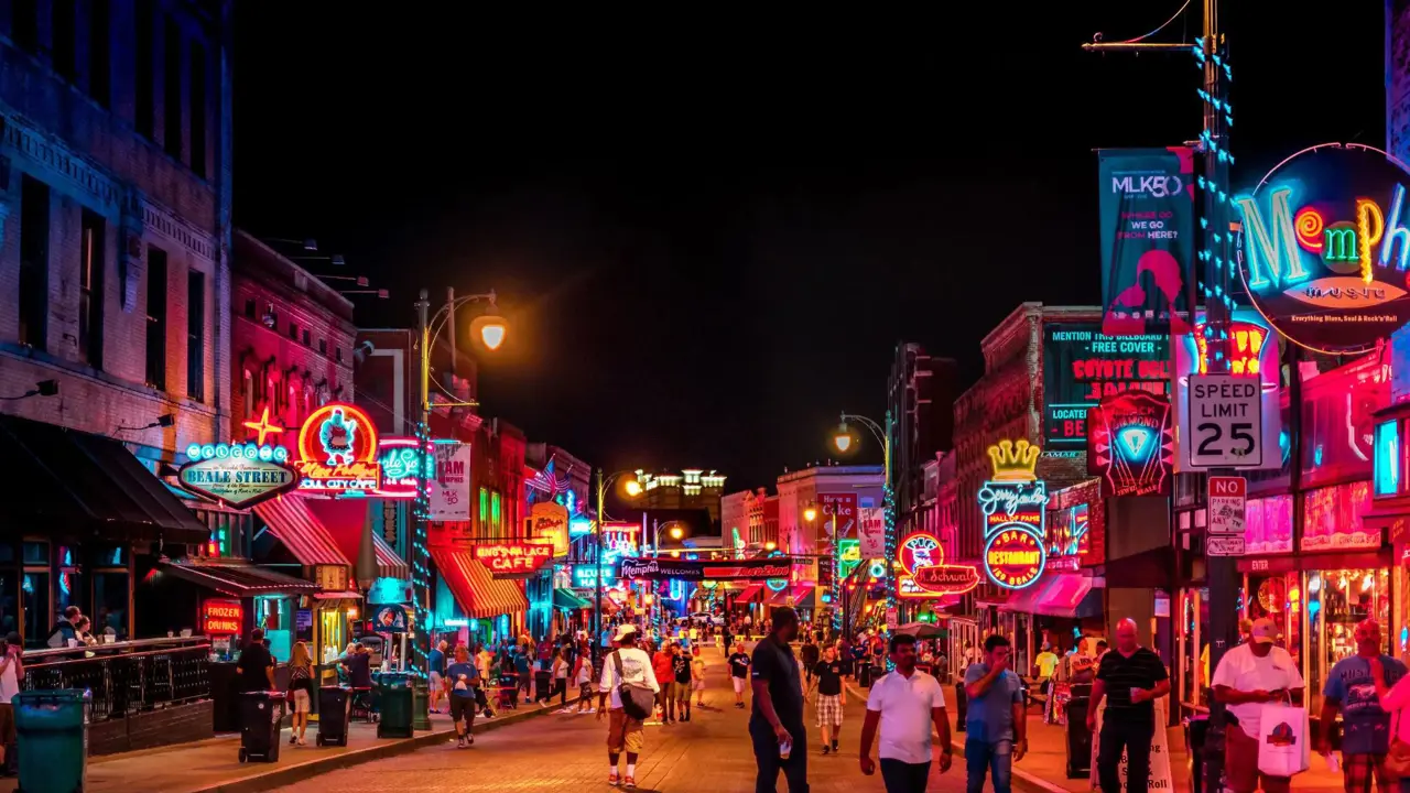 Vibrant night scene on Beale Street in Memphis, with neon signs glowing above blues clubs, bars, and live music venues, and crowds of people walking along the historic street
