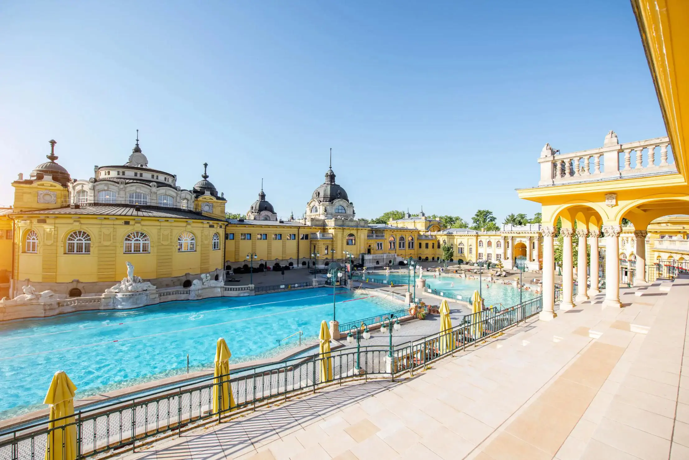 Two outdoor pools surrounded by grand yellow neo-baroque buildings on a sunny day at Széchenyi Thermal Baths in Budapest