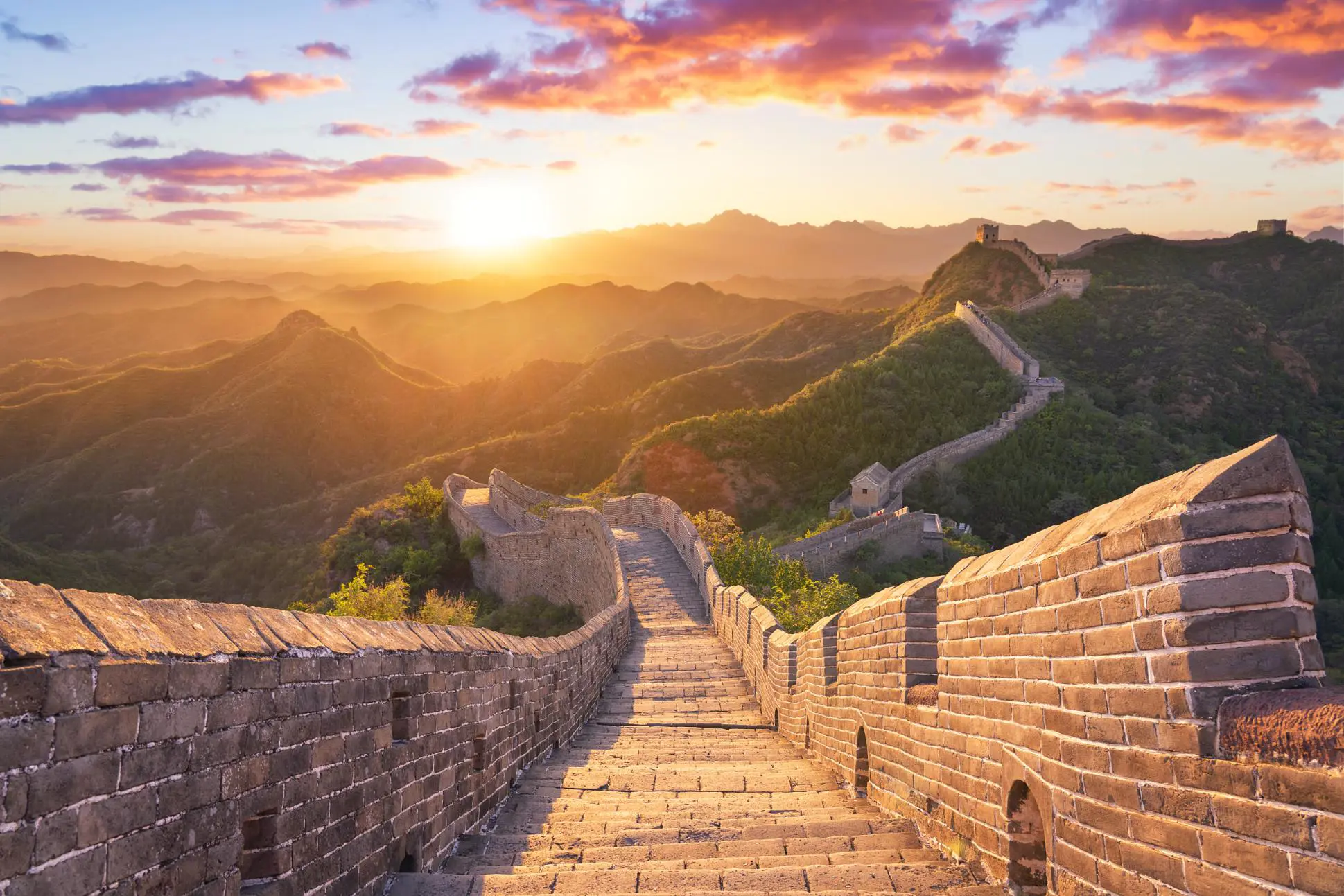 The Great Wall winding over mountain ridges, glowing in golden light at sunset, near Beijing, China