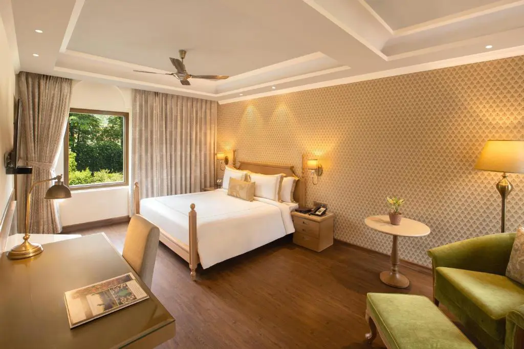 Bright hotel room at Heritage Village Resort And Spa in Gurugram, with a double bed, patterned wallpaper, desk and large window overlooking greenery