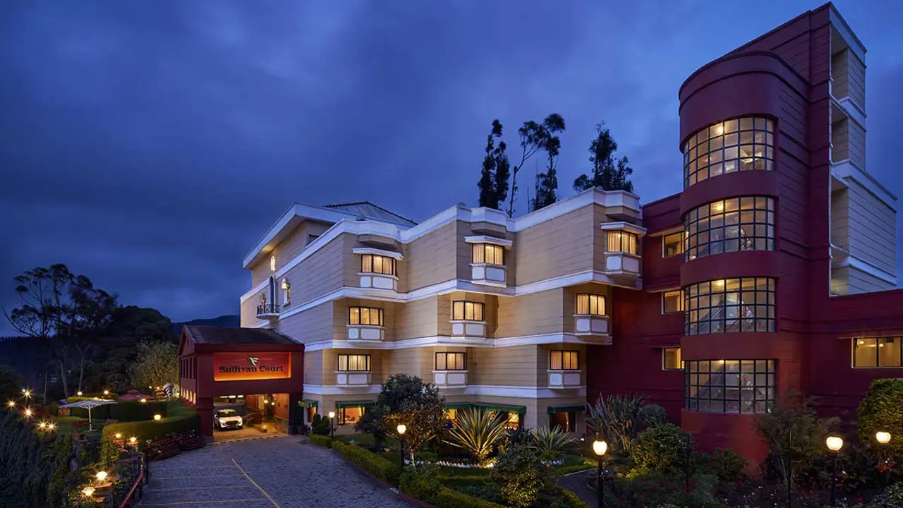 Fortune Resort Sullivan Court in Ooty, a charming hillside hotel with warm lighting, landscaped gardens, and classic cream and red architecture at dusk