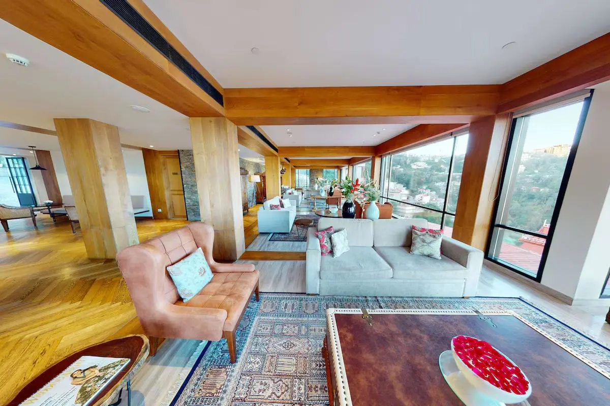 A bright lounge area with sofas, wooden beams and large windows overlooking hills at the Radisson Hotel Jass in Shimla