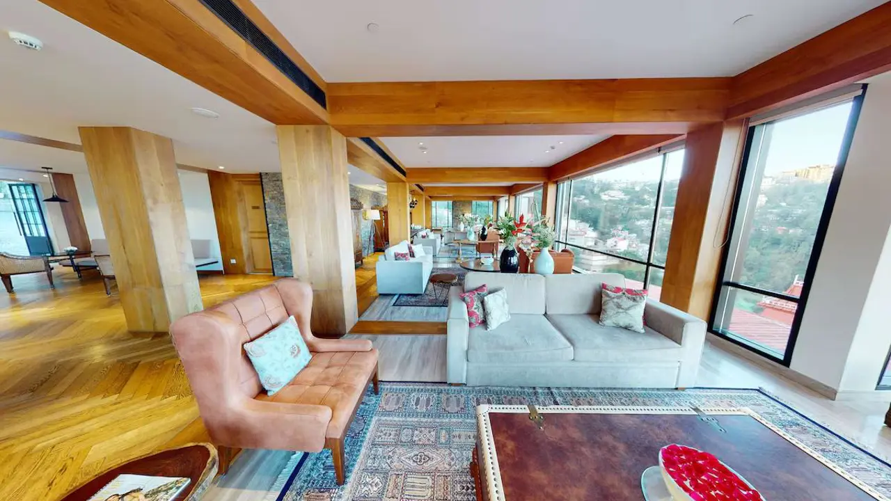 A bright lounge area with sofas, wooden beams and large windows overlooking hills at the Radisson Hotel Jass in Shimla