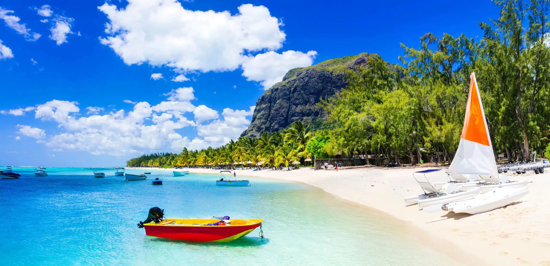 View of Mauritius featuring clear blue water, several boats floating on the sea, and a yacht on the sandy shore