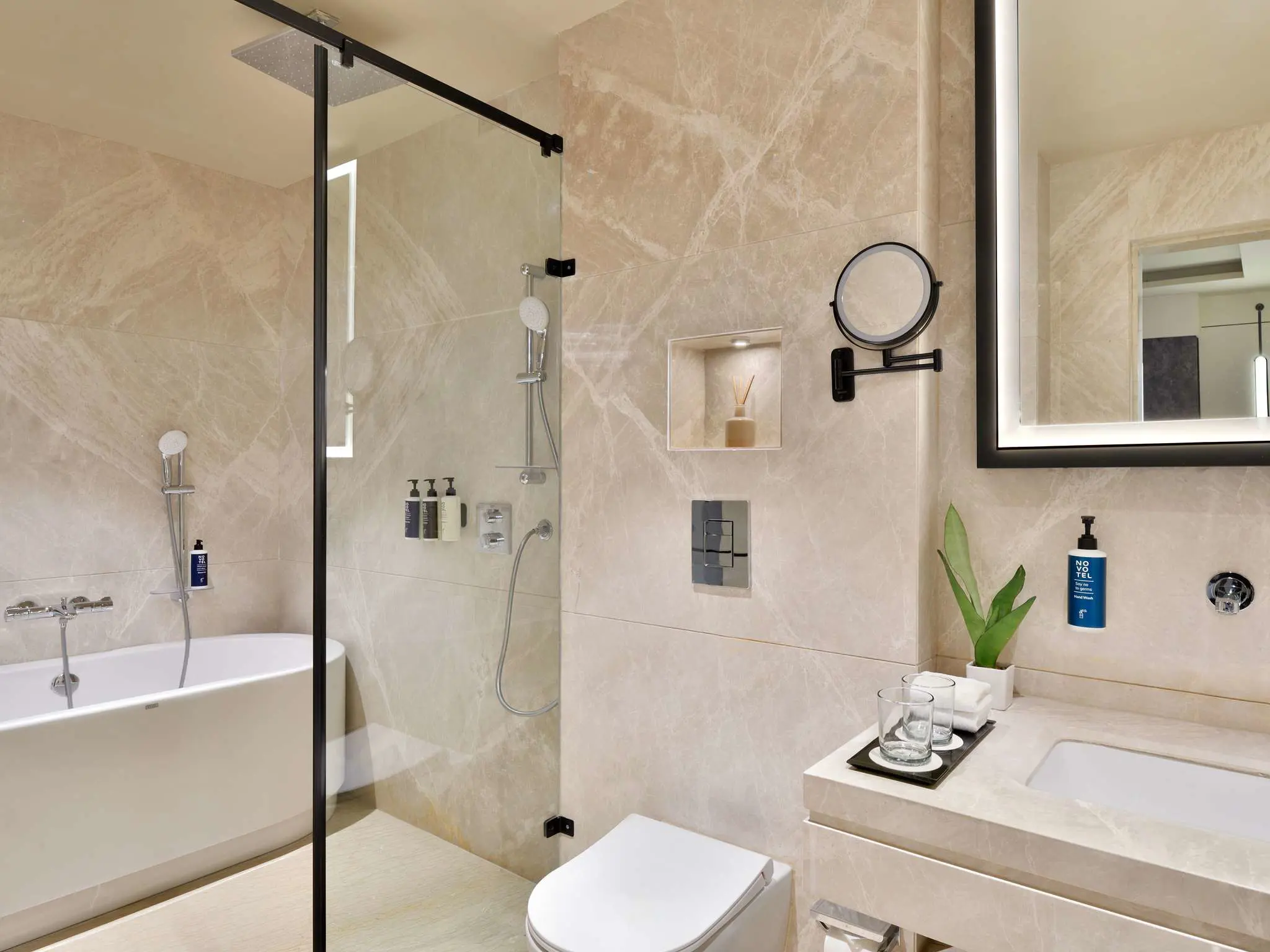 Modern bathroom at Novotel Jodhpur with a walk-in shower, bathtub, and beige marble tiles