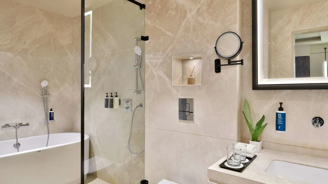 Modern bathroom at Novotel Jodhpur with a walk-in shower, bathtub, and beige marble tiles