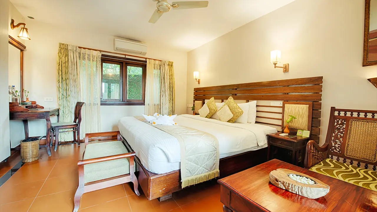 Brightly lit double guest room at Greenwoods Hotel in Periyar, featuring neutral décor, tiled flooring, and crisp white linens