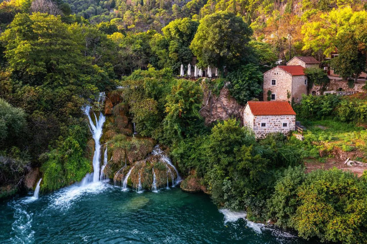 Aerial view of the beautiful Krka Waterfalls in Krka National Park on a bright summer morning with traditional small houses, green foliage and turquoise water