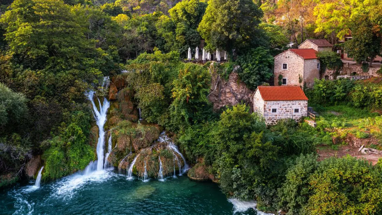 Aerial view of the beautiful Krka Waterfalls in Krka National Park on a bright summer morning with traditional small houses, green foliage and turquoise water