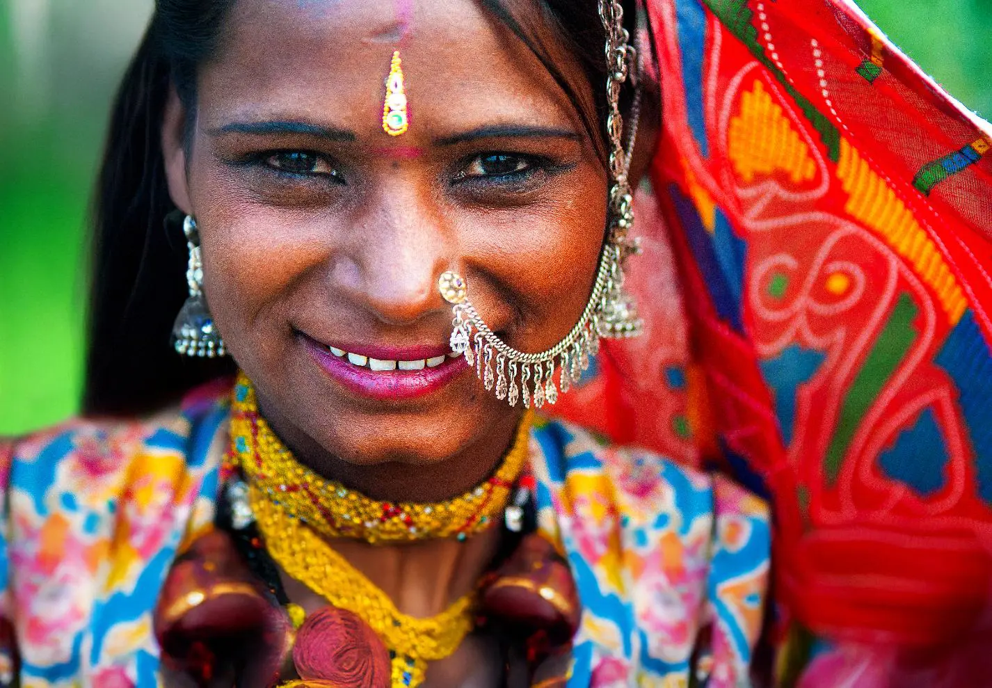 A close-up of a smiling Rajasthani woman dressed in vibrant traditional clothes and jewellery in Rajasthan in India