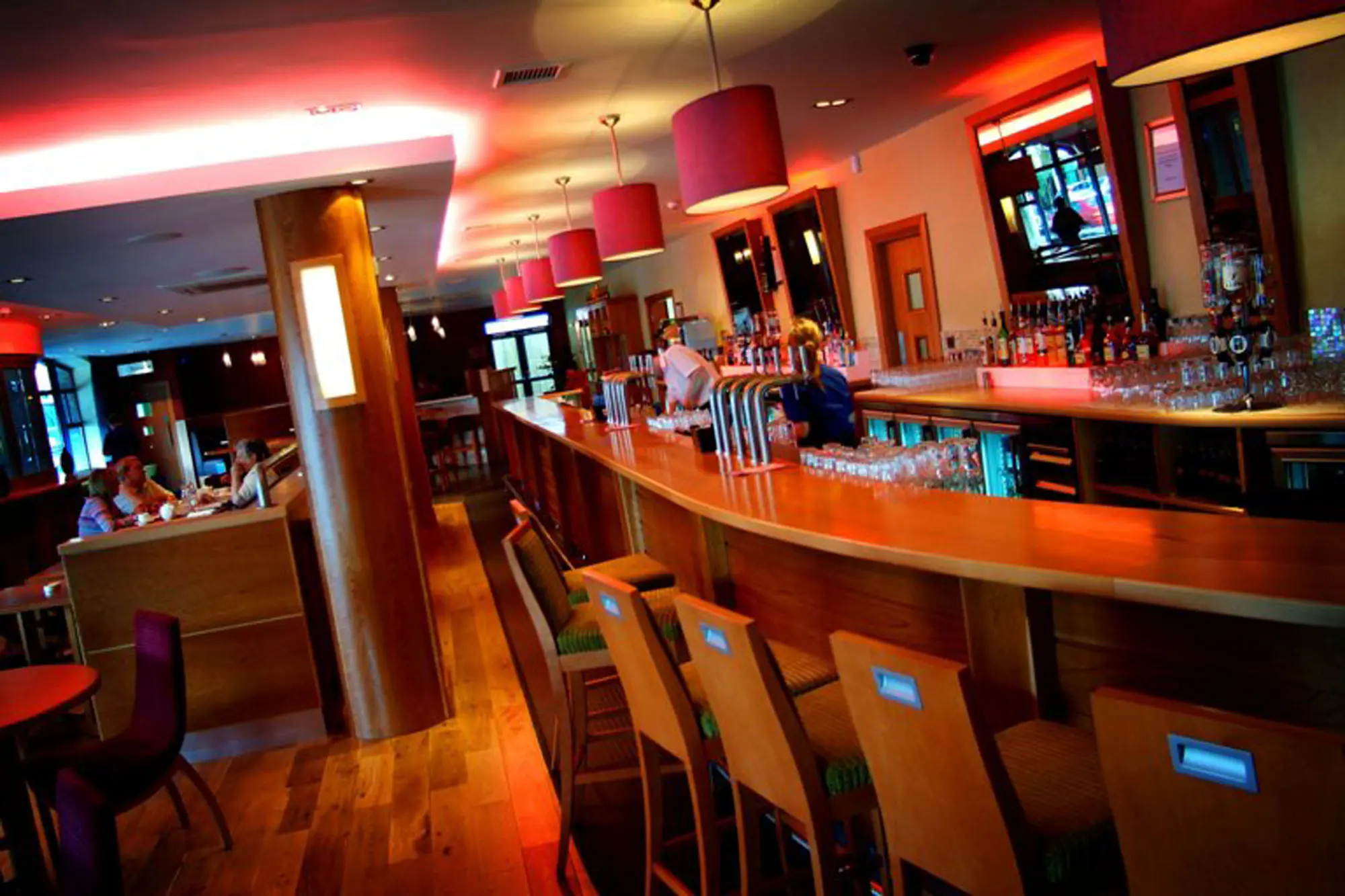 The Depot Bar at the Station House Hotel in Letterkenny, featuring a curved wooden bar, high stools, ambient red lighting, and cosy booth seating where guests are dining