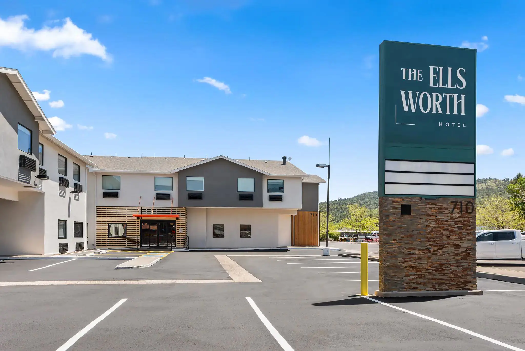 Exterior view of The Ellsworth Hotel, a modern building with large windows and a clean, welcoming façade, situated along a quiet street with clear skies overhead