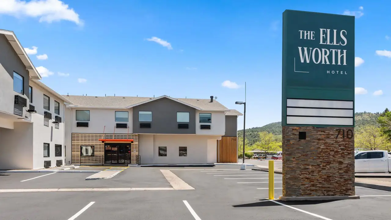 Exterior view of The Ellsworth Hotel, a modern building with large windows and a clean, welcoming façade, situated along a quiet street with clear skies overhead