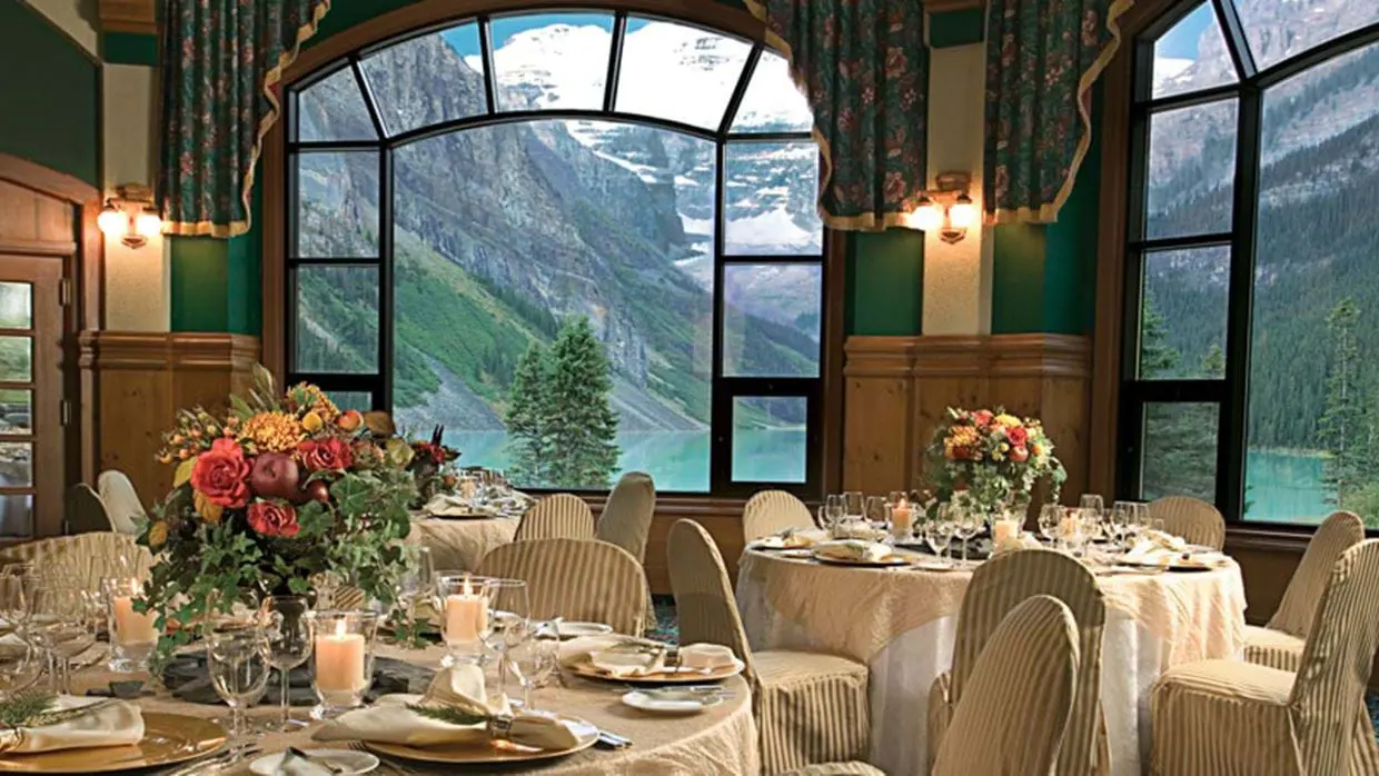 The elegant dining room at Fairmont Chateau with a view of Lake Louise and the Rocky Mountains through the arch windows