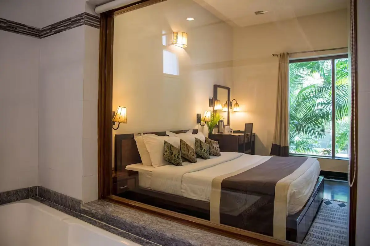 Elegant bedroom at Ranthambore Regency featuring a comfortable double bed, warm lighting and a large window overlooking lush greenery