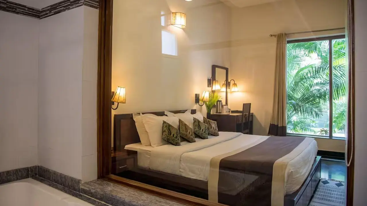 Elegant bedroom at Ranthambore Regency featuring a comfortable double bed, warm lighting and a large window overlooking lush greenery
