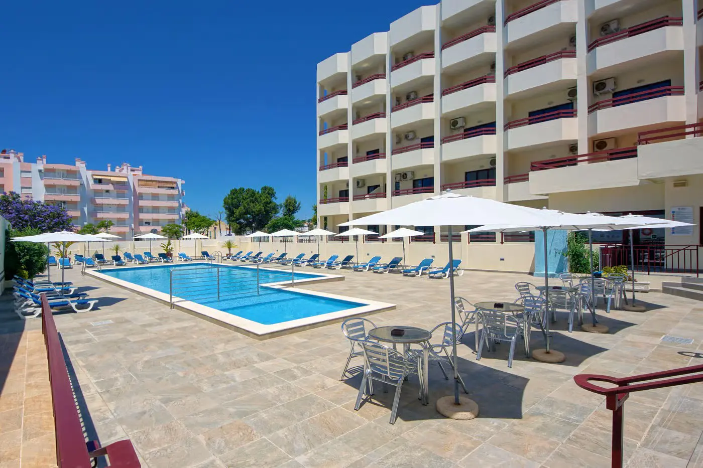 Outdoor pool at Hotel Alba in Portugal, surrounded by hotel room balconies, with sunloungers, tables, and chairs arranged around the poolside
