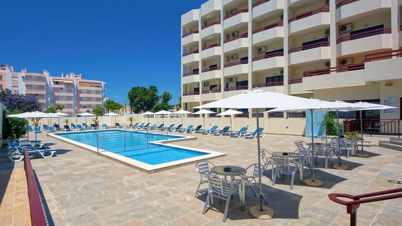 Outdoor pool at Hotel Alba in Portugal, surrounded by hotel room balconies, with sunloungers, tables, and chairs arranged around the poolside