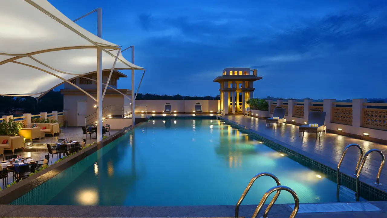 Outdoor rooftop swimming pool at the Grand Mercure Hotel in Mysore at dusk, with dining tables and chairs arranged around it