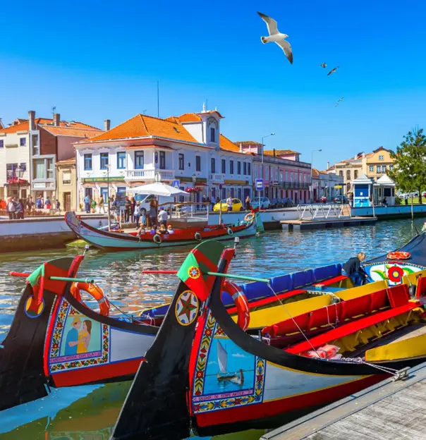 Brightly painted gondola-style boats moored along a canal lined with colourful buildings in Aveiro, Portugal