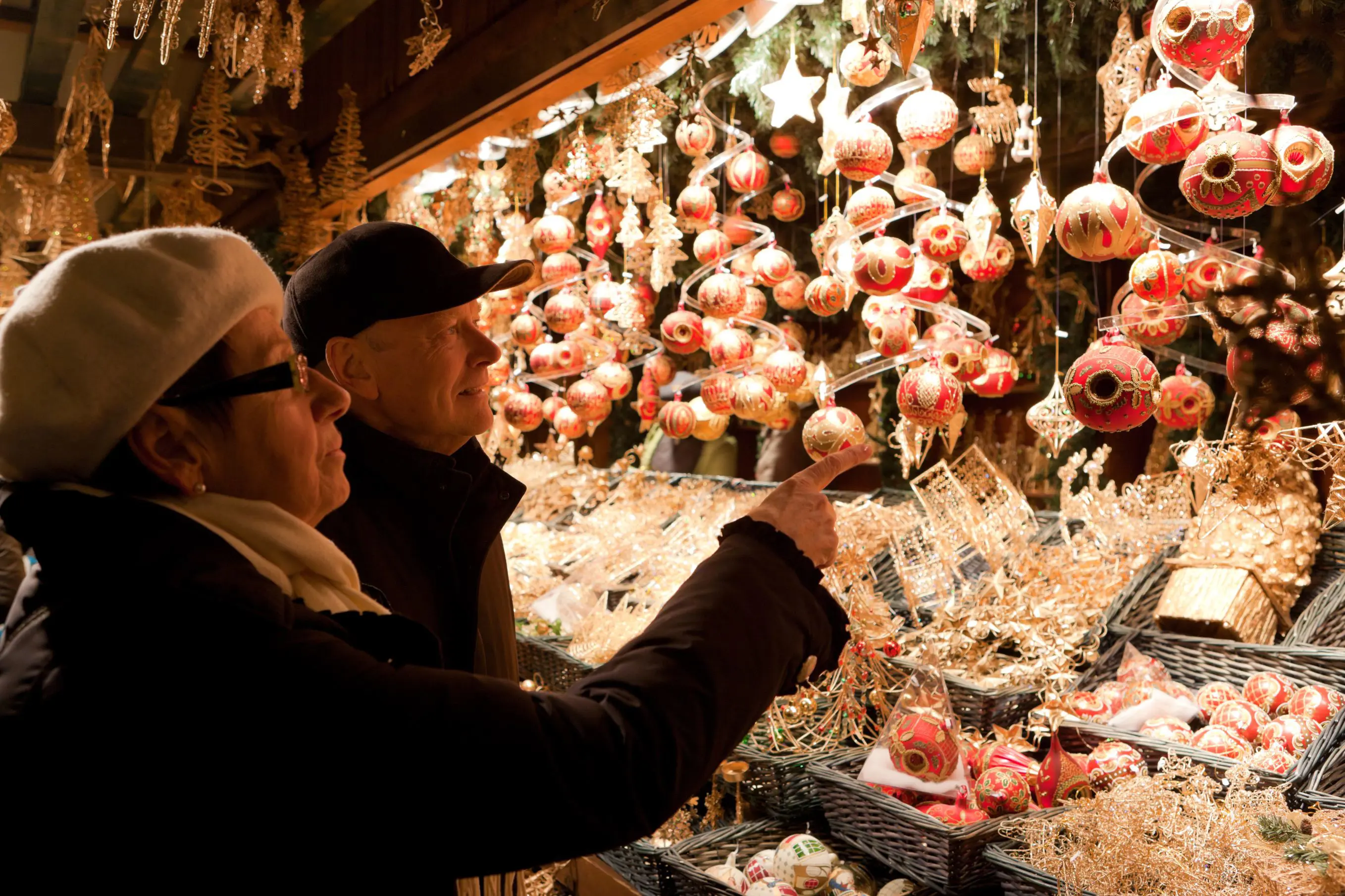 Mature couple looking at Christmas baubles being sold at a Christmas Market stall. The woman, who is in the forefront, is pointing towards one.
