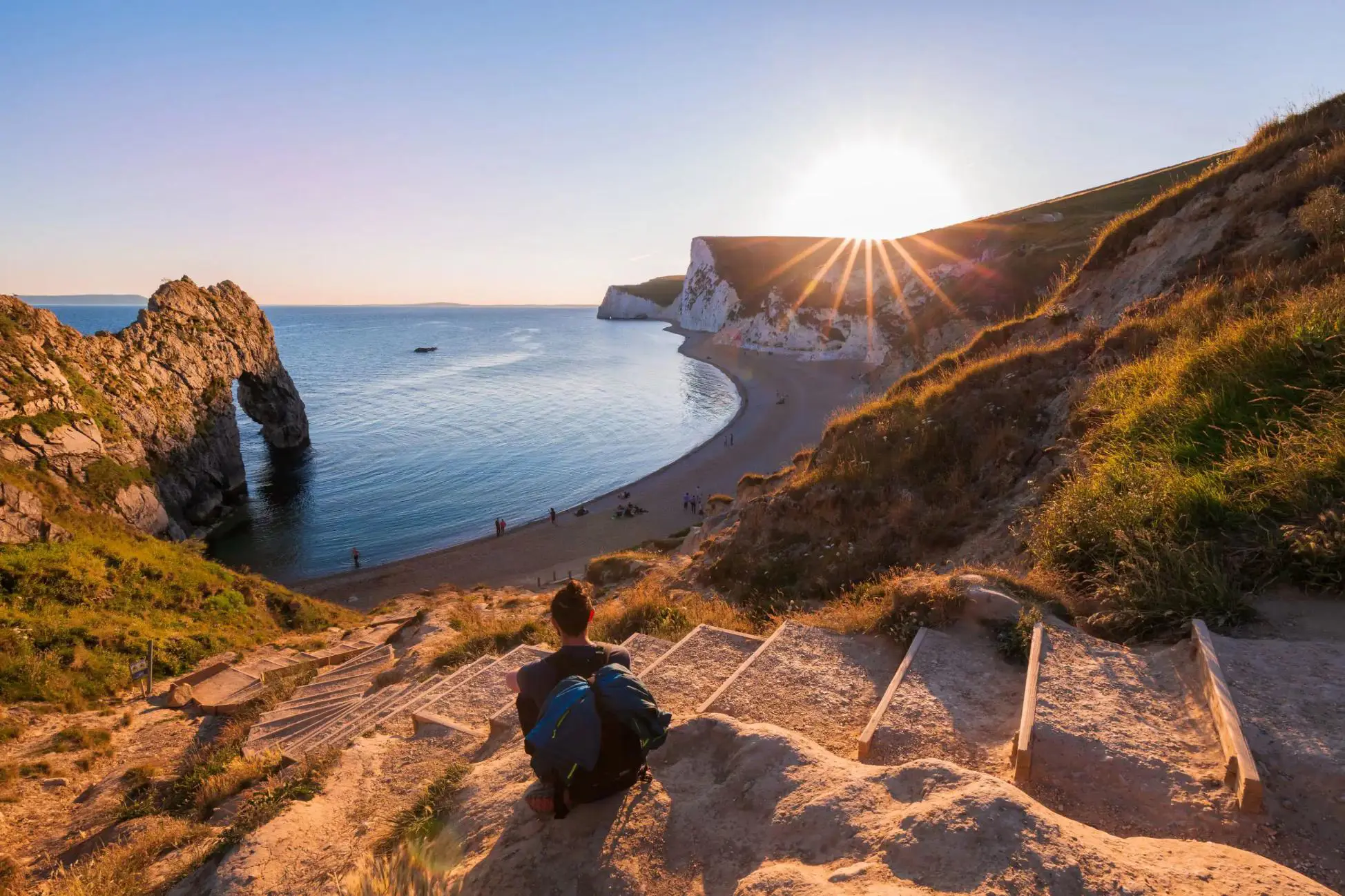 A person sitting on some steps overlooking the beach as the sunsets over the Jurassic Coast, Dorset 