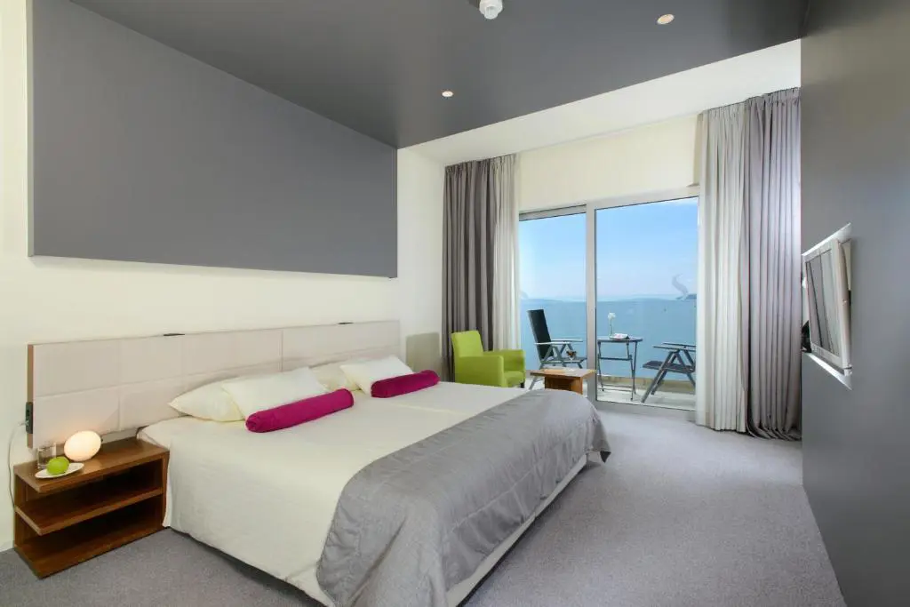 A contemporary room at Hotel Split, Podstrana, with a spacious double bed, sleek grey-and-white décor, and a private balcony offering uninterrupted views of the Adriatic Sea