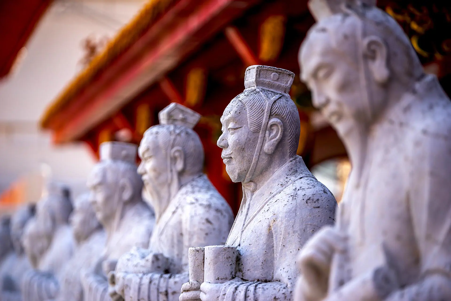 Stone statues of ancient scholars holding scrolls at the Confucius Temple in Nagasaki, Japan, with a red-roofed structure in the background