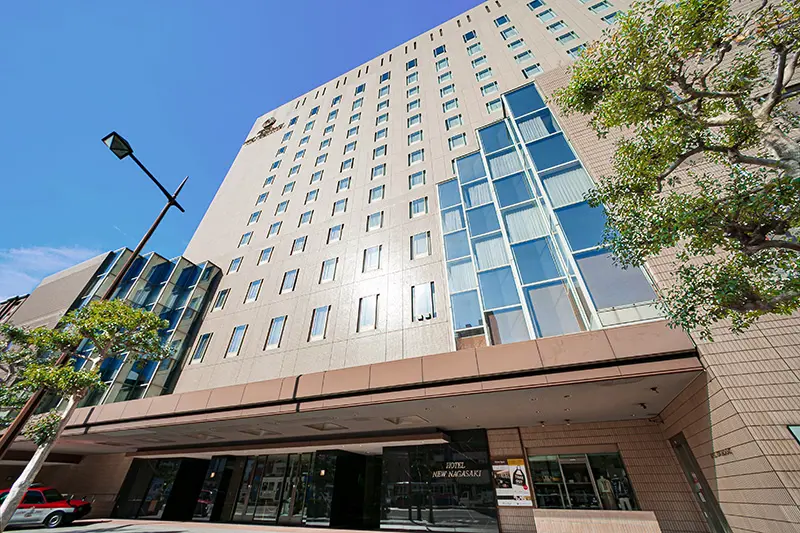 Exterior of Hotel New Nagasaki, a tall modern building with a light façade and rows of windows under a clear blue sky