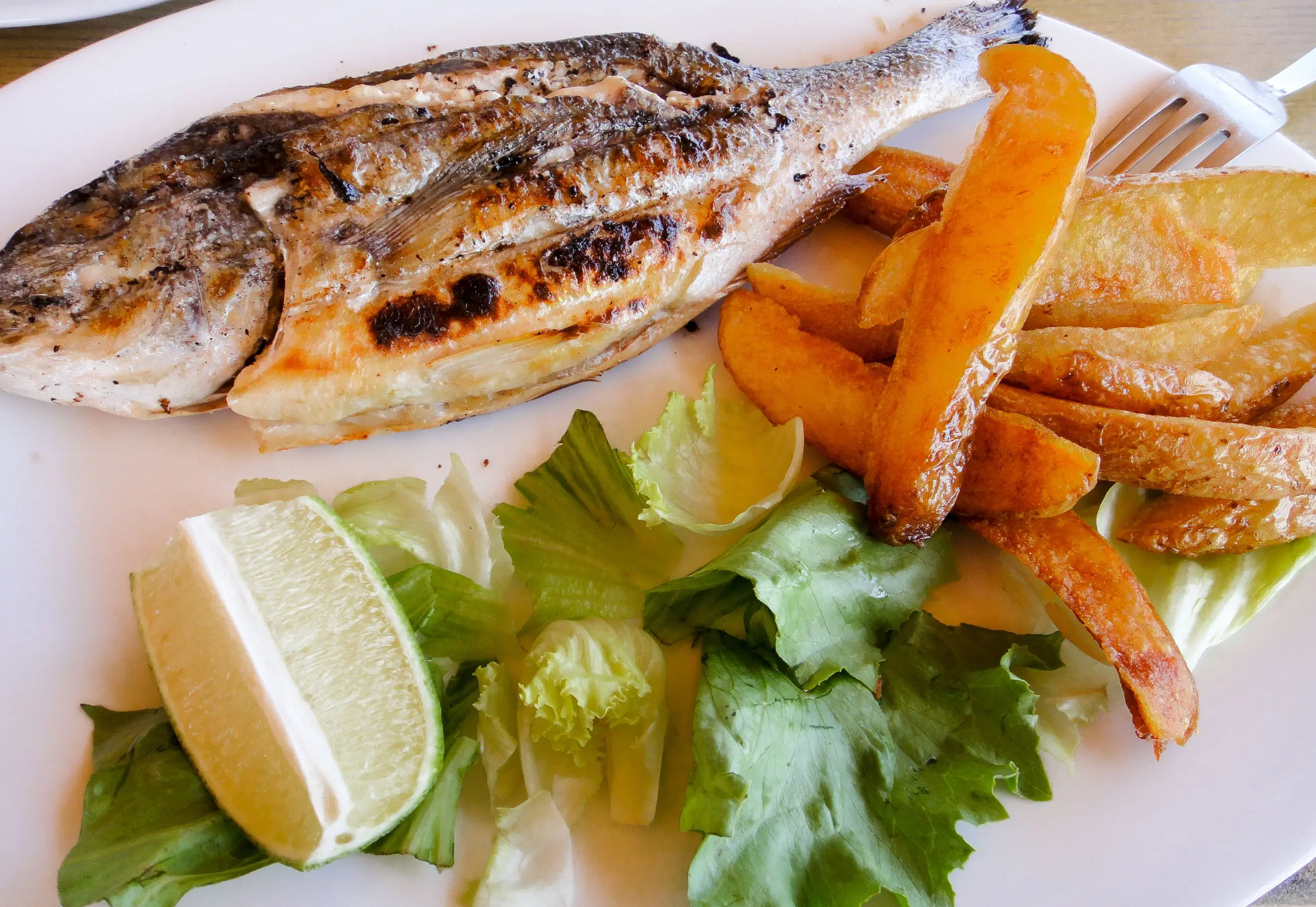 Close up of grilled fish, chips, some salad leaves and a wedge of lime. 