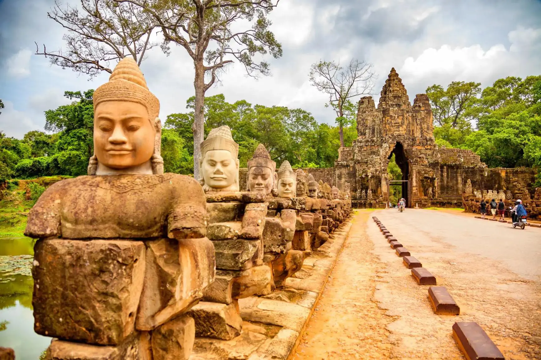 Stone statues line the entrance road to the majestic Angkor Thom gate, surrounded by dense green jungle