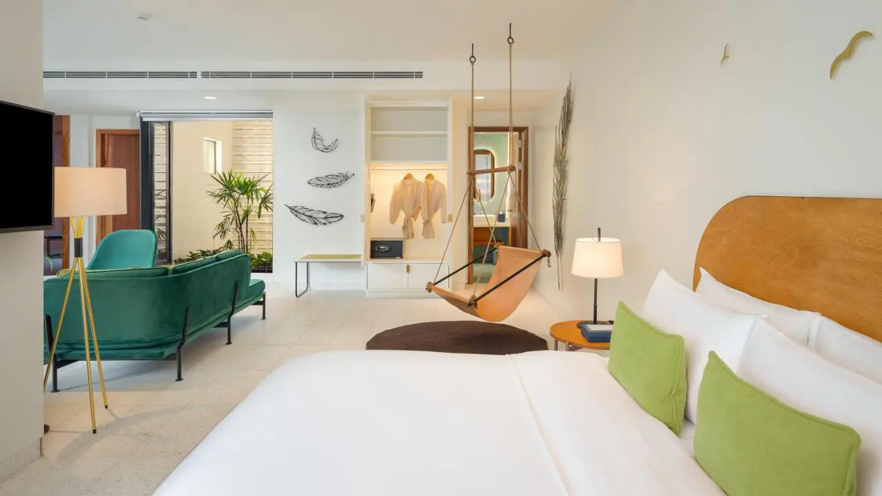 Spacious studio room at The Aviary Hotel, Siem Reap, featuring a comfortable bed, a seating area, and modern wooden furnishings
