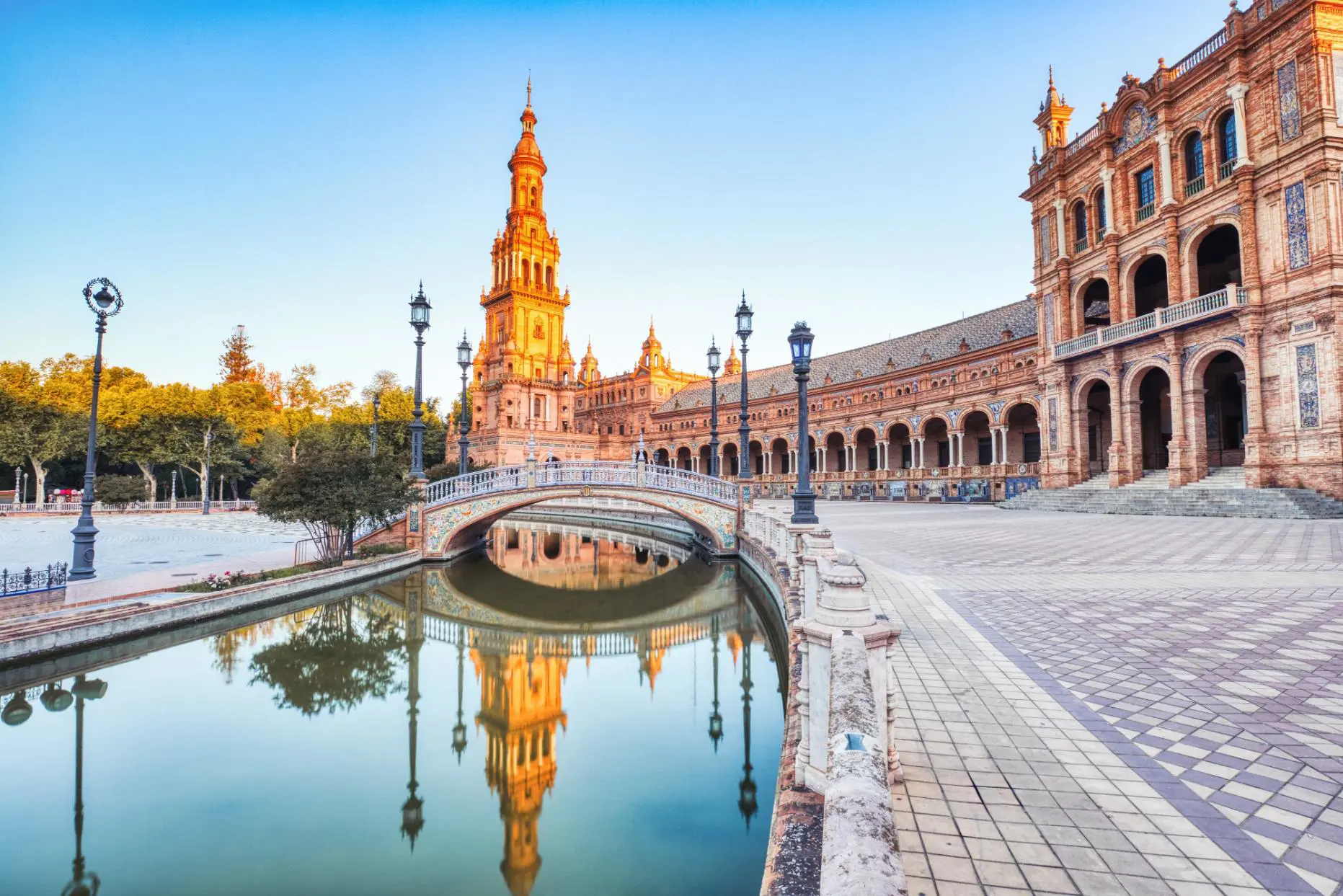 View of Plaza de España in Seville showing the tower, ornate tilework, and a small river with a bridge crossing it