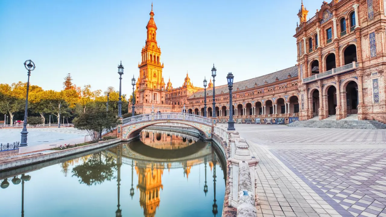 View of Plaza de España in Seville showing the tower, ornate tilework, and a small river with a bridge crossing it