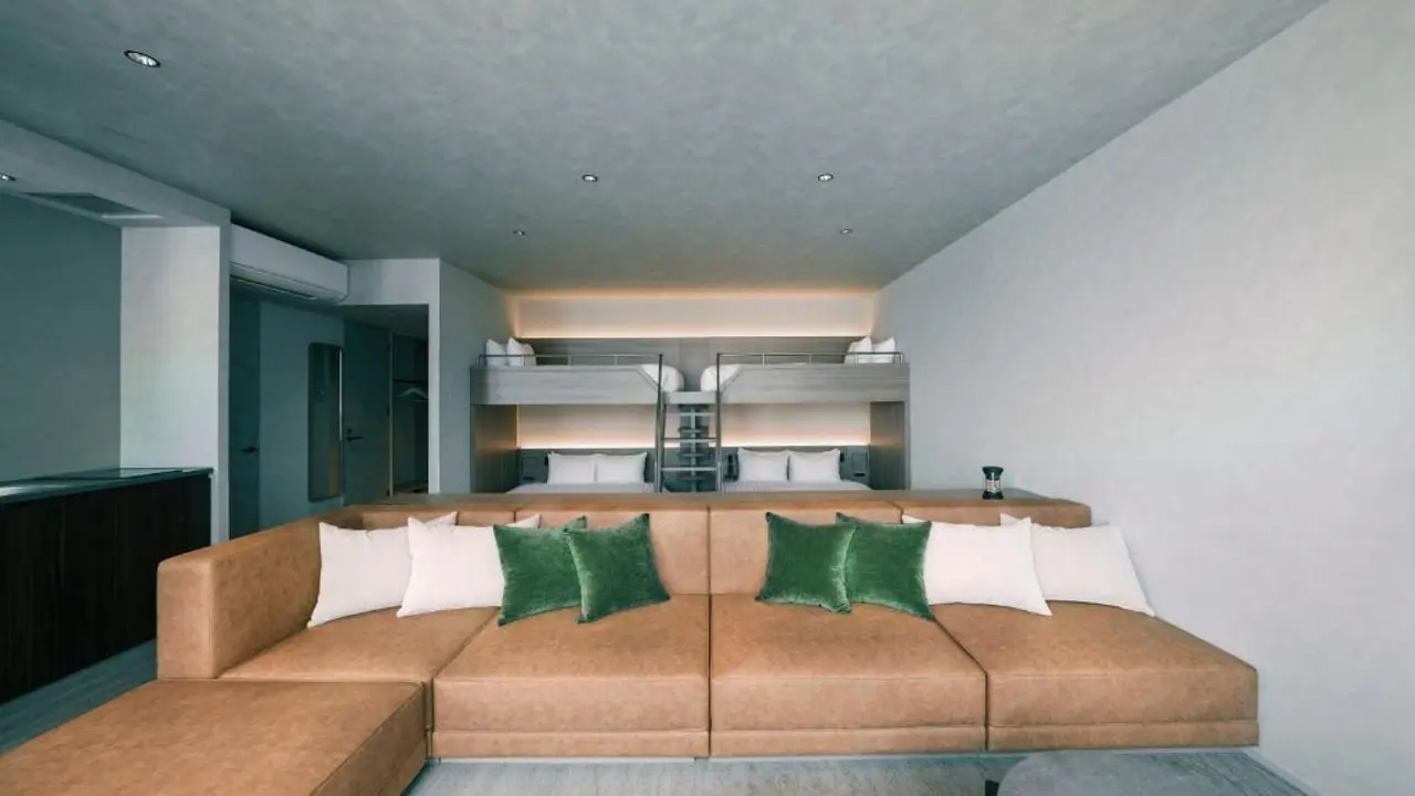Spacious suite at FAV LUX Nagasaki featuring a large tan sectional sofa with green cushions and bunk beds in the background