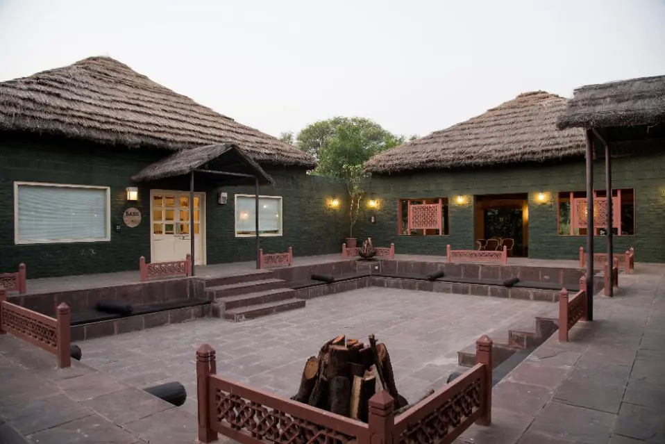 Traditional courtyard at Vannashyra Cottages with stone flooring, thatched-roof buildings, central fire pit, and cushioned seating