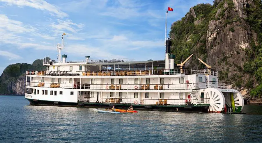 The Emeraude Classic Cruise, a vintage-style white paddle steamer with green trim, anchored in the emerald waters of Ha Long Bay