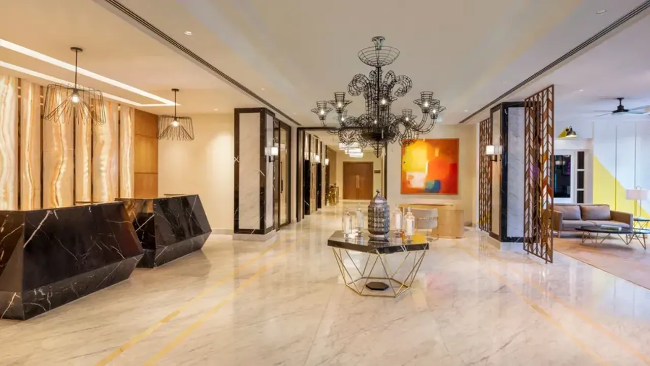 Bright reception area at The Residency Towers hotel in Pondicherry, featuring white marble floors, two check-in desks, and a decorative chandelier at the centre of the room