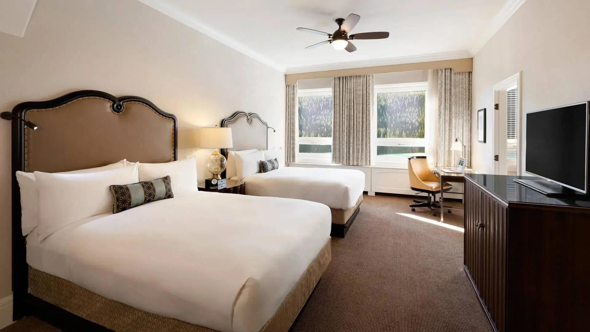 A twin room at Fairmont Chateau, Lake Louise in a warm modern style with two double beds and a mountain view