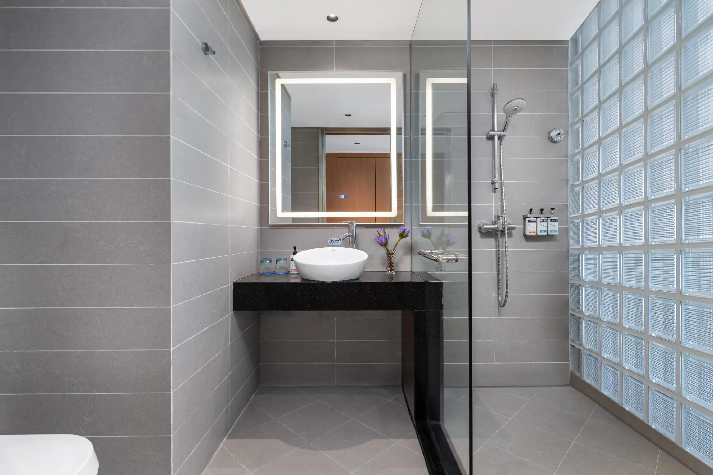 A stylish bathroom at the Holiday Inn Express Chengdu Gulou, designed with grey tiles, a glass-enclosed shower, a backlit mirror, and modern fittings for a clean, sophisticated look