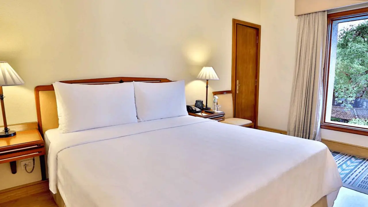 Classic double guest room at The Fern hotel in Kochi, featuring white linens, soft wooden furnishings, and warm lighting