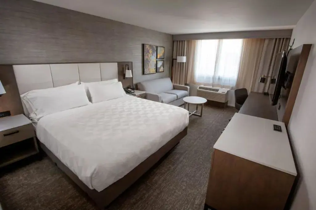 Spacious and modern king room at the DoubleTree by Hilton Buena Park, featuring a large bed with crisp white linens, a work desk, lounge chair, and contemporary décor in neutral tones