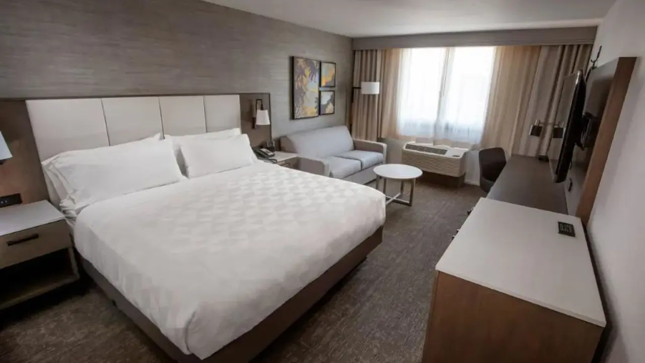 Spacious and modern king room at the DoubleTree by Hilton Buena Park, featuring a large bed with crisp white linens, a work desk, lounge chair, and contemporary décor in neutral tones