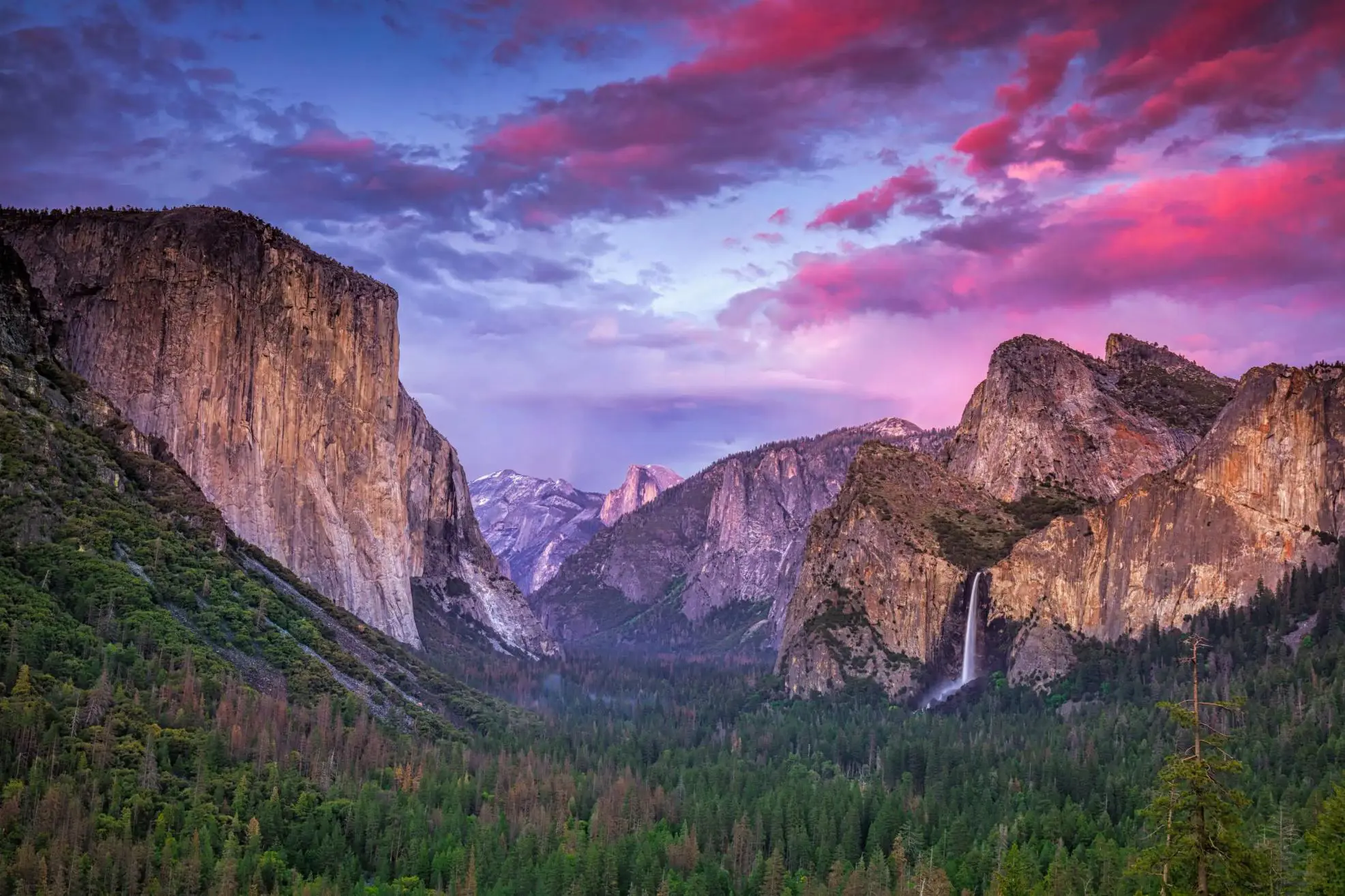 Breathtaking view of Yosemite National Park, California, featuring towering granite cliffs and lush green forests beneath a pink and blue sky at sunset