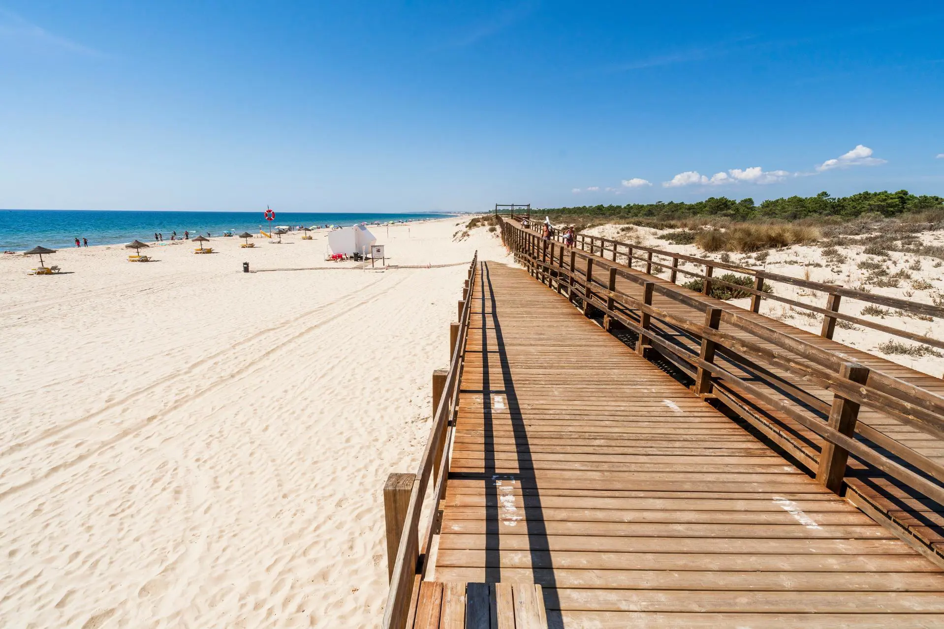 Wooden walkway on the beach at Monte Gordo on the Algarve, with the sandy beach and sea to the left and a shrub area to the right