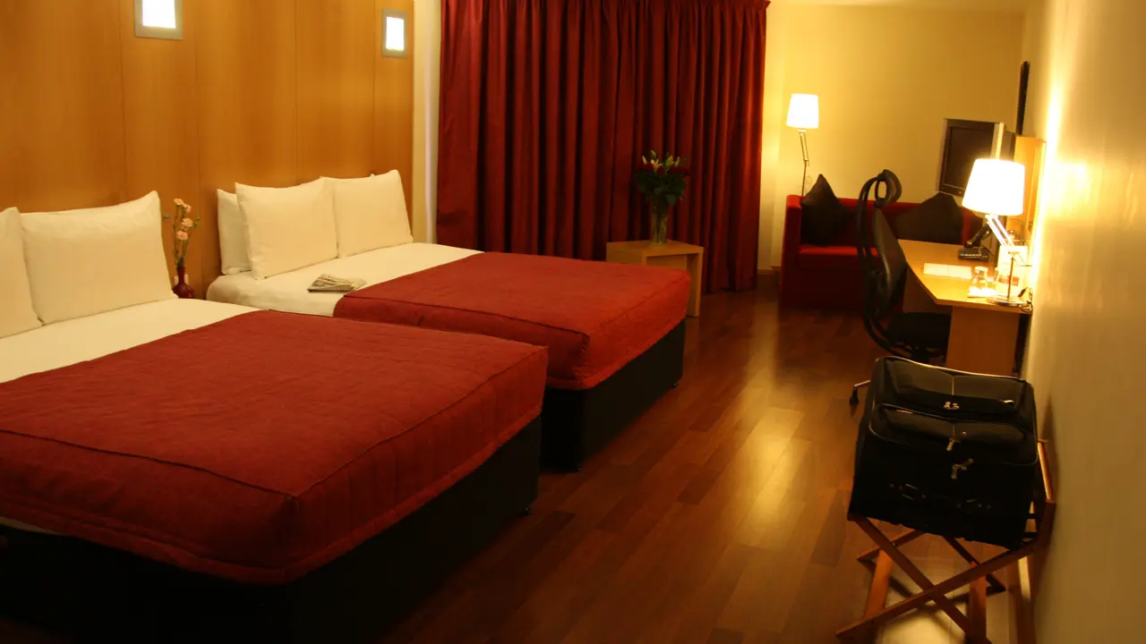 Modern hotel room at Station House Hotel, Letterkenny featuring two double beds, wooden floors, desk, TV, and a cosy seating area with armchair