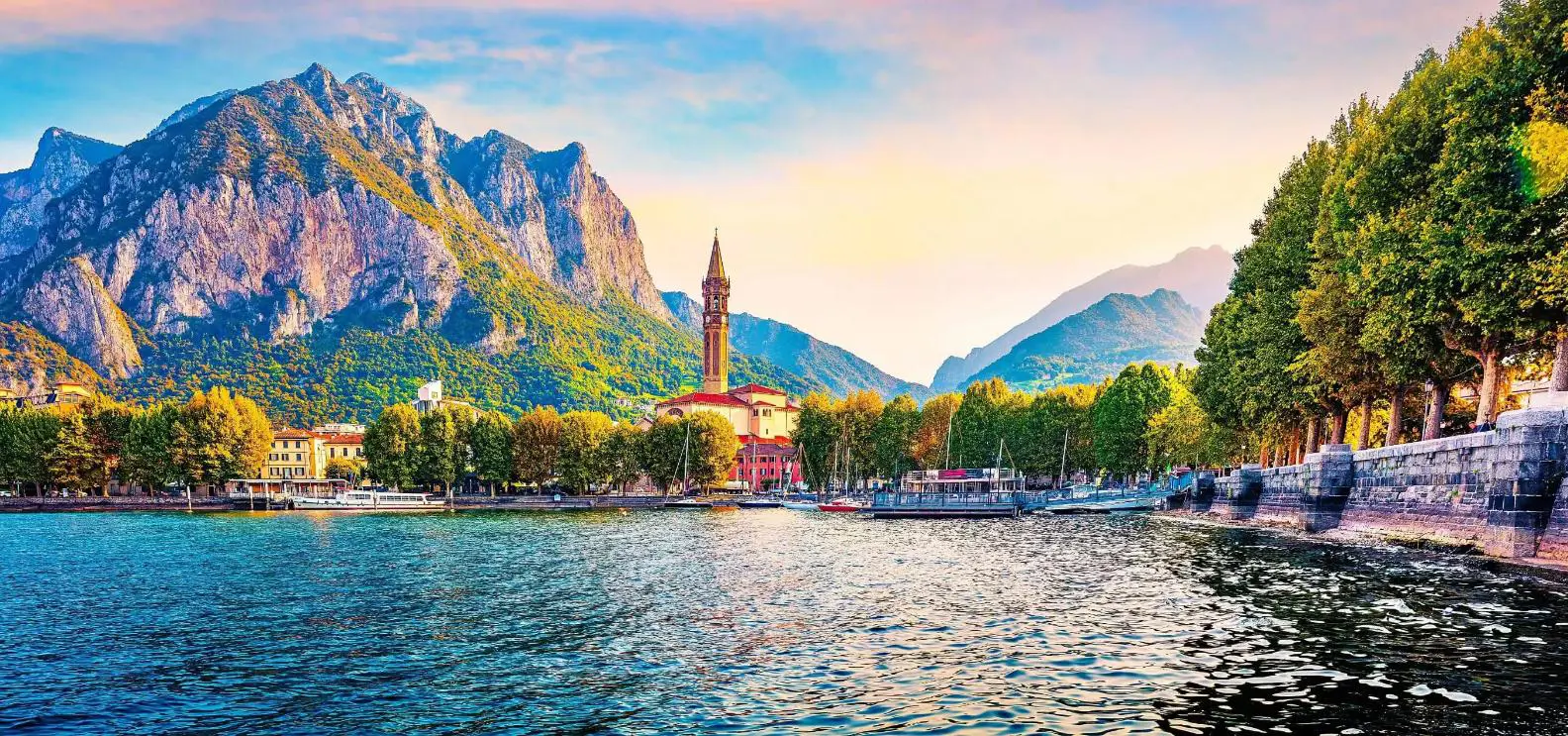 A view of Lake Como with a small church tower and mountains and trees in the background